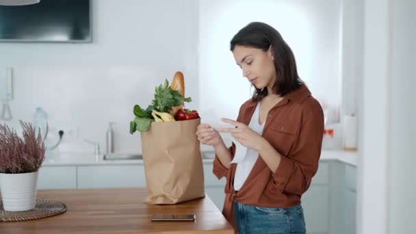 自宅のキッチンで食料品の領収書を見ている美しい若い女性のビデオ — ストック動画