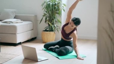 Spor yapan genç bir kadının yoga egzersizleri yaptığı video evde dizüstü bilgisayarla beden eğitimi derslerini takip ediyor..