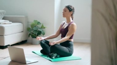 Spor yapan genç bir kadının yoga egzersizleri yaptığı video evde dizüstü bilgisayarla beden eğitimi derslerini takip ediyor..