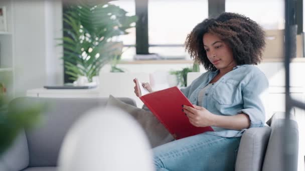 自宅でソファーに座ってリラックスしながら本を読んでいる美しいスマートな女性のビデオ — ストック動画