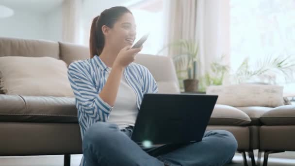 一个漂亮的年轻女人坐在家里用手机和笔记本电脑一起工作的视频 — 图库视频影像