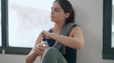 Spor salonundaki spor salonundan sonra protein içeceği içen genç bir kadının evinde yerde otururken videosu.