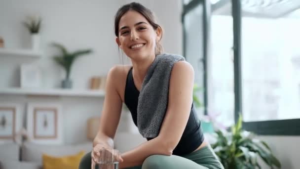 自宅に座っている一杯の水を飲みながら運動から休憩を取るスポーティな女性のビデオ — ストック動画