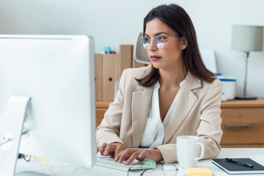Ofiste bilgisayarla çalışan zarif ve zeki bir iş kadınının fotoğrafı.