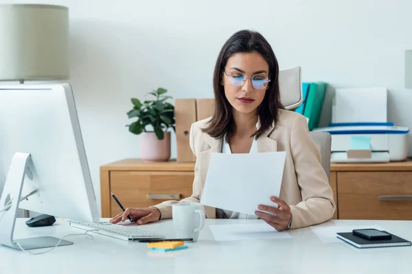 オフィスでいくつかのノートを読みながらコンピュータで作業するエレガントなスマートビジネス女性のショット — ストック写真
