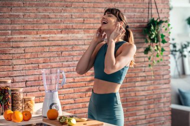 Mutfakta şarkı söyleyip müzik dinlerken sağlıklı bir şekilde smoothie içen güzel bir kadın..