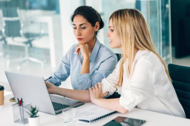 Shot of two elegant businesswomen talking while working together in a modern startup clipart