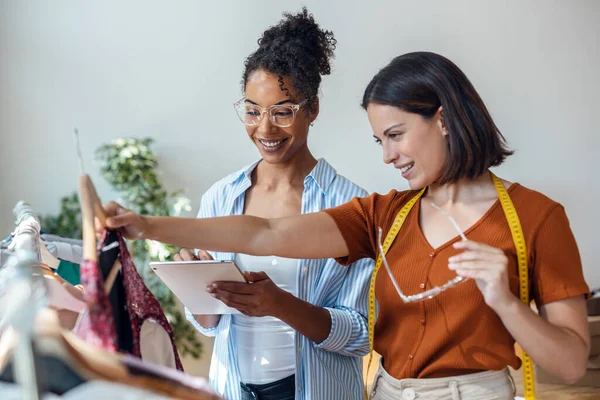 stock image Shot of two fashion designers working while taking notes of clothes with digital tablet in the sewing workshop