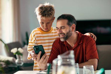 Yakışıklı baba ve tatlı oğlu öğle yemeğinden önce evde akıllı telefon kullanıyor.
