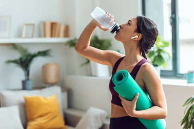 Spor salonunda su içen güzel bir kadının evde beden dersinden önce kulaklıkla müzik dinlemesi.