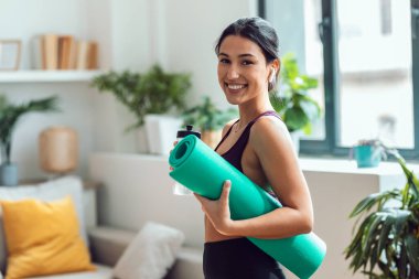Spor salonunda su içen güzel bir kadının evde beden dersinden önce kulaklıkla müzik dinlemesi.