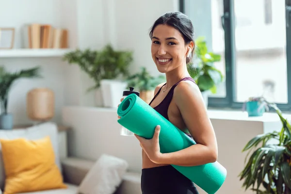 stock image Shot of sporty beautiful woman drinking water while listening music with earphones before gym class at home