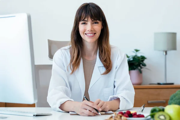 stock image Shot of beautiful smart nutritionist woman working with computer while looking at camera in the nutritionist consultation