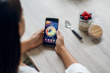 Sportif bir kadının evdeki mutfakta akıllı telefonlu beslenme uygulaması kullanarak arka plan görüntüsü.
