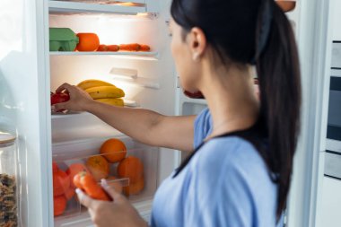 Mutfaktaki buzdolabının önünde yemek yemeye çekinen genç ve güzel bir kadın..