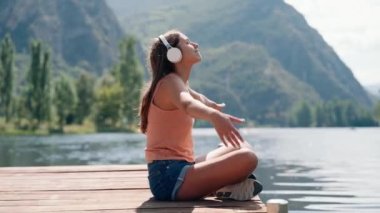 Güzel bir kadının, gölün kenarında oturup kulaklıkla müzik dinlediği bir video.