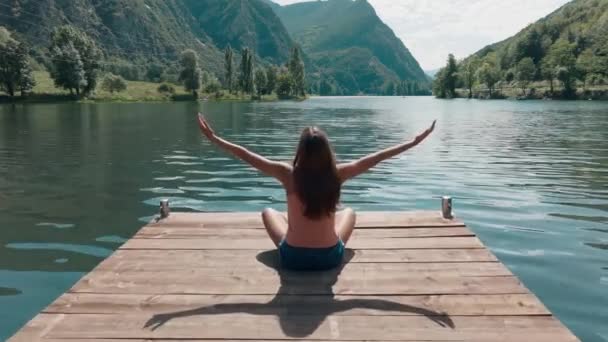 湖の近くに座っている彼の腕を上げながらリラックスしている若い女性の無人機のビデオ — ストック動画