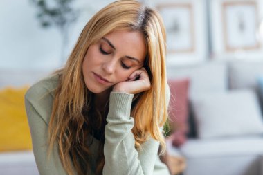 Evdeki oturma odasında sorunlarını düşünen güzel endişeli genç bir kadının portresi.