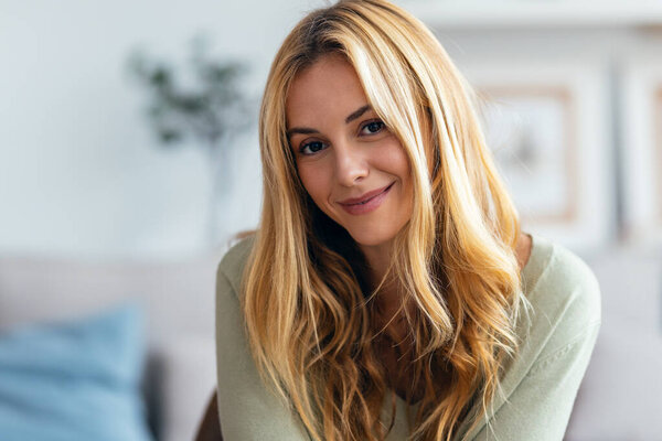 Портрет доброй молодой женщины, позирующей, глядя на камеру в гостиной дома.