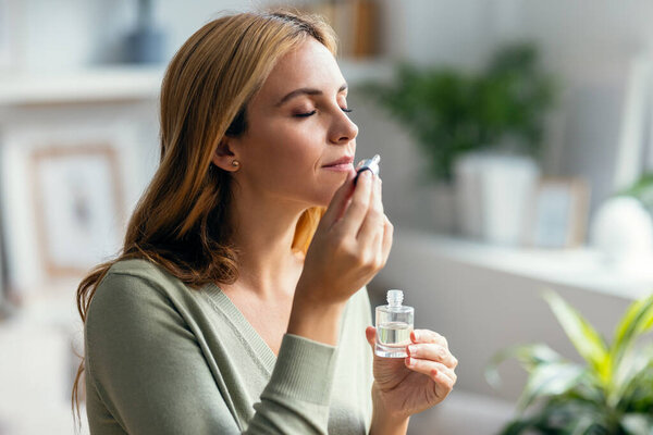 Shot of a beautiful woman holding a bottle of essential oil while testing it sitting on a couch at home.