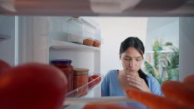 Mutfaktaki buzdolabının önünde yemek yemeye çekinen güzel bir genç kadının videosu.