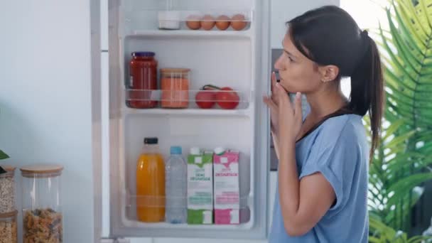 Video Van Mooie Jonge Vrouw Aarzelend Eten Voor Koelkast Keuken — Stockvideo