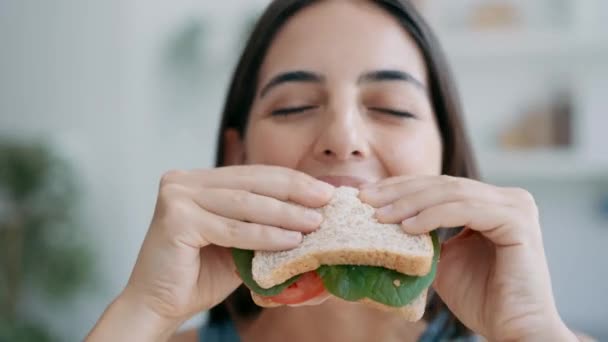 自宅のキッチンでカメラを見ながら健康的なサンドイッチを食べる美しいスポーティな女性のビデオ — ストック動画