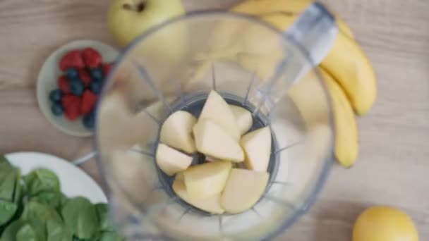 キッチンでデトックスジュースを準備するためのブレンダーに野菜や果物の種類の異なる種類を置くかなり若い女性のビデオ — ストック動画