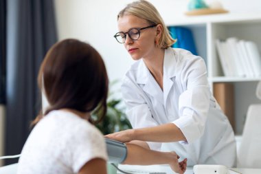 Tıbbi muayenede genç bir hastayla ilgilenirken kalp ve kan basıncını ölçen olgun kadın doktor iğnesi.