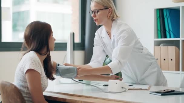 医療相談で若い患者にケアしながら心臓と血圧を測定する成熟した女性医師のビデオ — ストック動画