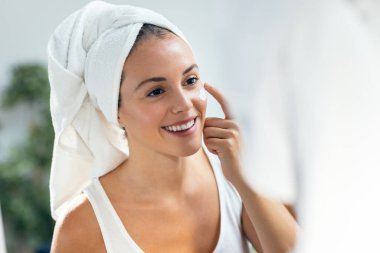 Evdeki aynaya bakarken cildine özen gösteren güzel genç bir kadının portresi..