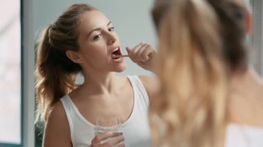 Evdeki banyoda aynaya bakarken dişlerini fırçalayan genç bir kadının videosu..