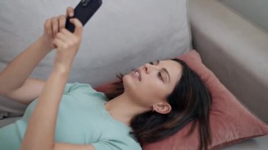 Evdeki kanepede uzanırken cep telefonuyla mesaj gönderen güzel bir genç kadının videosu..