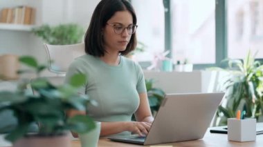 Video of concentrated beautiful business woman working with laptop while drinking coffee in living room at home.
