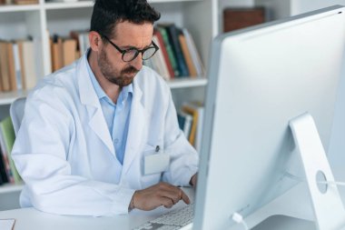 Tıbbi konsültasyonda notlar yazarken bilgisayarla çalışan olgun bir erkek doktorun fotoğrafı.