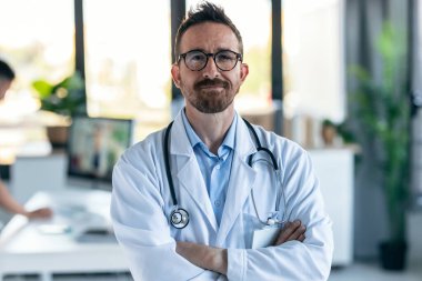 Tıbbi muayenede kameraya bakarken boynunda steteskop olan yetişkin bir erkek doktorun portresi..