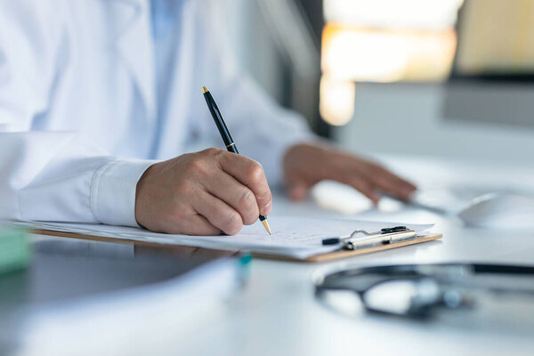 Shot of mature male doctor with stethoscope over neck taking notes in clipboard in a medical consultation