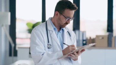 Boynunda steteskop olan yetişkin bir erkek doktorun tıbbi muayenede not aldığı bir video.