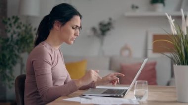 Evdeki oturma odasında sorun yaşarken dizüstü bilgisayarla çalışan endişeli iş kadını videosu.