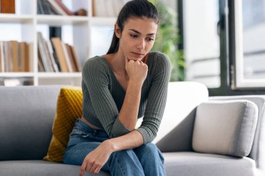 Evdeki kanepede otururken sorunlarını düşünen depresif bir genç kadın..