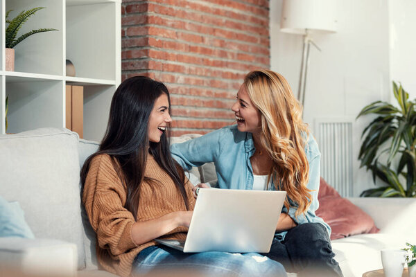 Shot of two happy beautiful women doing a video call with laptop sitting on the couch at home.