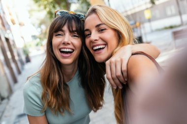 Gece şehirde barış jesti gösterirken iki neşeli kadının akıllı telefonuyla selfie çekmesi.