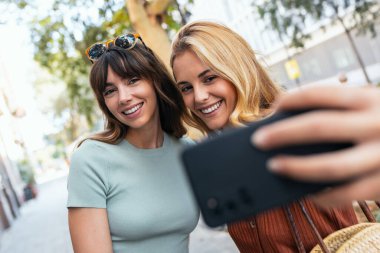 Gece şehirde barış jesti gösterirken iki neşeli kadının akıllı telefonuyla selfie çekmesi.