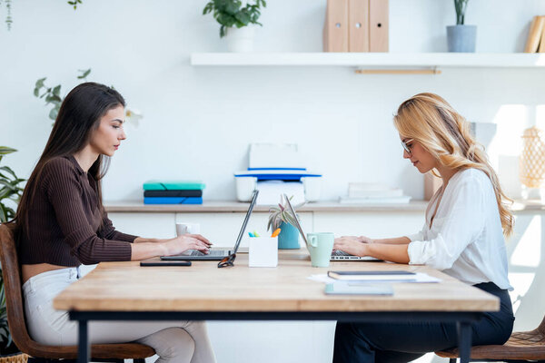 Shot of two elegant attractive businesswomen talking while working together with laptop in a modern startup