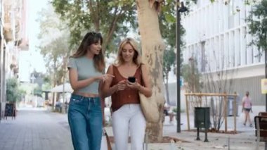İki güzel arkadaşın alışveriş çantasıyla sokakta yürürken konuştuğu ve akıllı telefon kullandığı bir video..