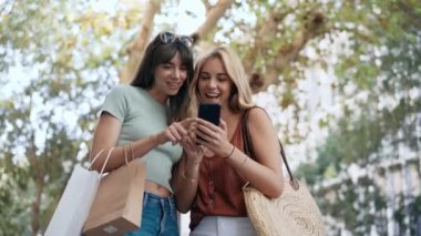 İki güzel arkadaşın alışveriş çantasıyla sokakta yürürken konuştuğu ve akıllı telefon kullandığı bir video..