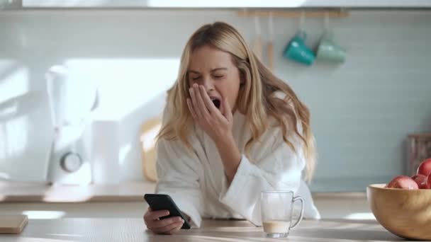 自宅のリビングルームで携帯電話を使ってコーヒーを楽しんでいる若い女性の笑顔のビデオ — ストック動画