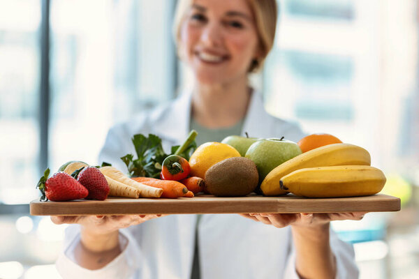 Close-up of beautiful smiling nutritionist holding wooden table with fresh fruits and vegetables in a medical consultation