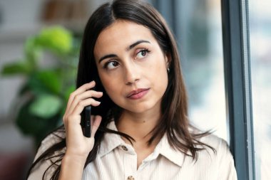 Kendine güvenen bir kadının evinin penceresinin yanında dikilirken cep telefonuyla konuşması.