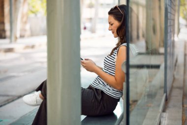 İstasyonda tramvayı beklerken cep telefonunu kullanan neşeli bir kadın.